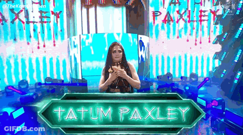 A Woman Is Standing In Front Of A Sign That Says Tatum Paxley On It . GIF
