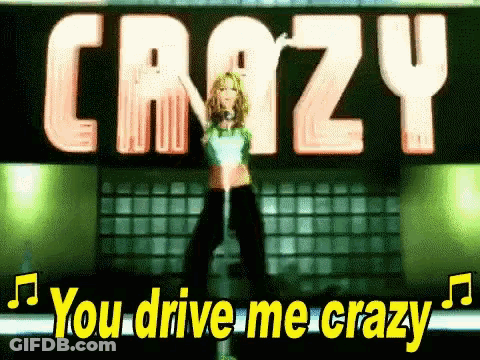A Woman Is Standing In Front Of A Sign That Says `` You Drive Me Crazy '' While Holding A Microphone . GIF