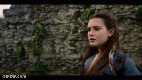 A Woman Is Standing In Front Of A Stone Wall And Looking At The Camera . GIF