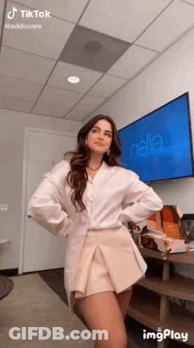 A Woman Is Standing In Front Of A Television With The Name Addisonre On It GIF