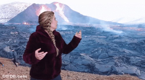 A Woman Is Standing In Front Of A Volcano GIF