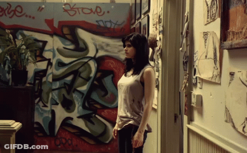 A Woman Is Standing In Front Of A Wall With Graffiti On It That Says " Steve " GIF