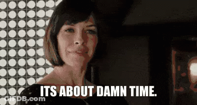A Woman Is Standing In Front Of A Wall With Polka Dots And Says `` It 'S About Damn Time . '' GIF