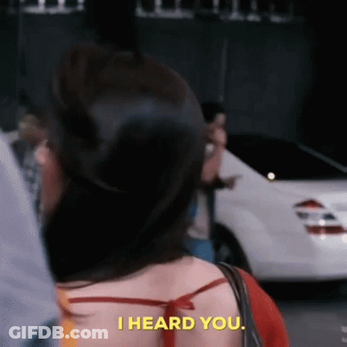 A Woman Is Standing In Front Of A White Car And Saying `` I Heard You . '' GIF