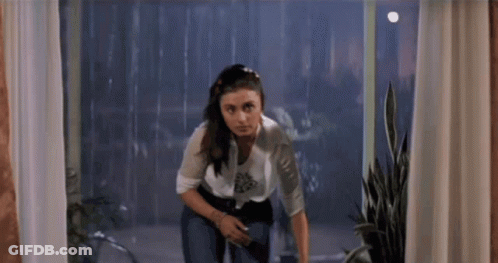 A Woman Is Standing In Front Of A Window Looking Out GIF