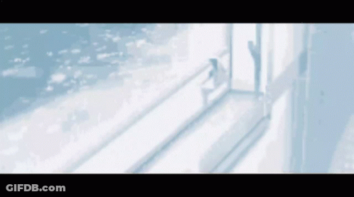 A Woman Is Standing In Front Of A Window Looking Out At The Ocean . GIF