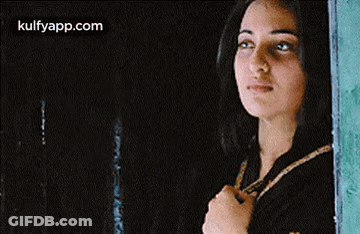 A Woman Is Standing In Front Of A Window Looking Out . GIF