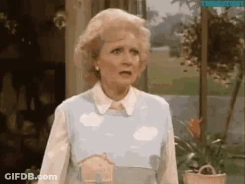A Woman Is Standing In Front Of A Window Wearing A Blue Sweater With Clouds On It . GIF