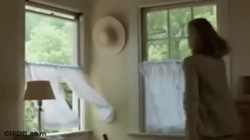 A Woman Is Standing In Front Of A Window With A Hat On The Wall GIF