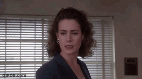 A Woman Is Standing In Front Of A Window With Blinds . GIF