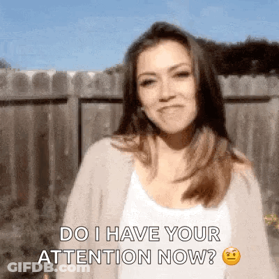 A Woman Is Standing In Front Of A Wooden Fence And Says Do I Have Your Attention Now . GIF