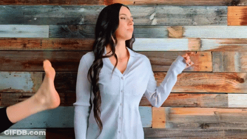 A Woman Is Standing In Front Of A Wooden Wall GIF