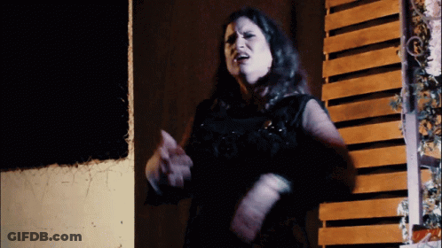 A Woman Is Standing In Front Of A Wooden Wall GIF