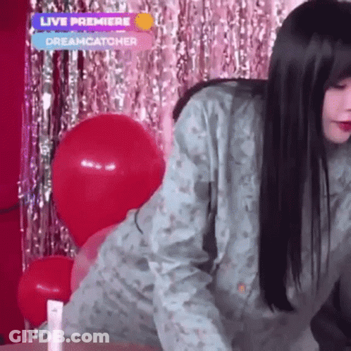 A Woman Is Standing In Front Of Balloons And A Live Premiere Sign GIF