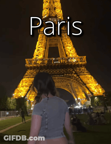 A Woman Is Standing In Front Of The Eiffel Tower At Night With The Word Paris Above Her GIF