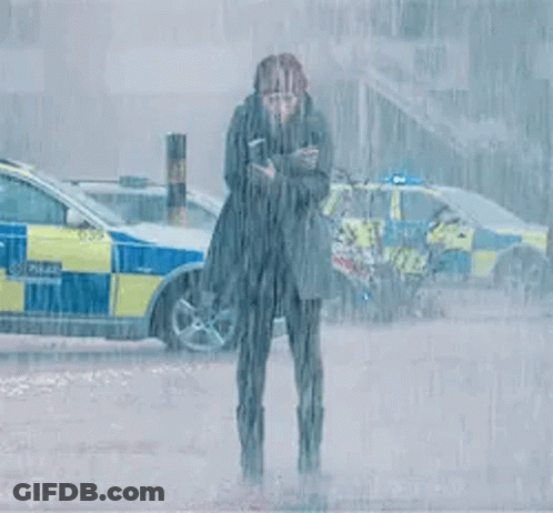 A Woman Is Standing In The Rain In Front Of A Police Car Holding A Cell Phone . GIF