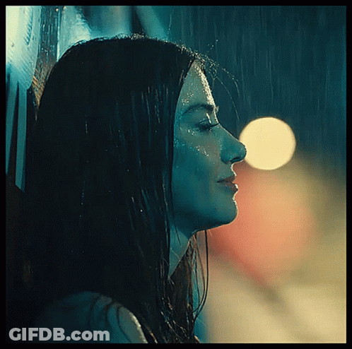 A Woman Is Standing In The Rain With Her Eyes Closed GIF