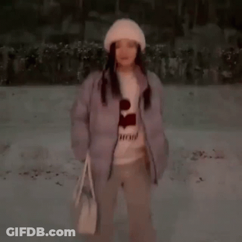 A Woman Is Standing In The Snow Wearing A Hat And A Sweater . GIF