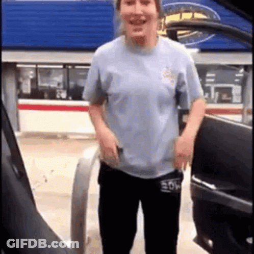 A Woman Is Standing Next To A Car At A Gas Station And Smiling . GIF