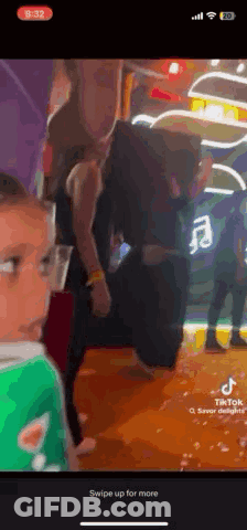 A Woman Is Standing Next To A Child In A Green Shirt In A Room . GIF