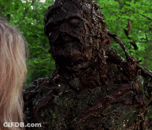 A Woman Is Standing Next To A Statue Of A Monster Covered In Mud GIF
