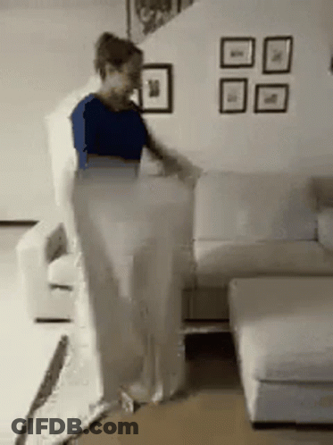 A Woman Is Standing Next To A White Couch In A Living Room GIF