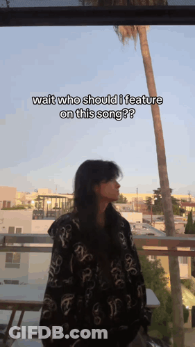 A Woman Is Standing On A Balcony With The Caption Wait Who Should I Feature On This Song ? GIF