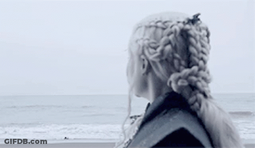 A Woman Is Standing On A Beach Looking At The Ocean . GIF