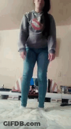 A Woman Is Standing On A Bed Wearing A Hoodie And Jeans . GIF