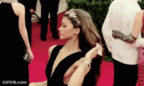A Woman Is Standing On A Red Carpet Adjusting Her Hair . GIF