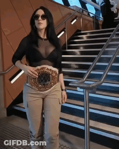 A Woman Is Standing On A Set Of Stairs Holding A Wrestling Belt On Her Waist . GIF