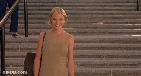 A Woman Is Standing On A Set Of Stairs Smiling And Holding A Bag . GIF