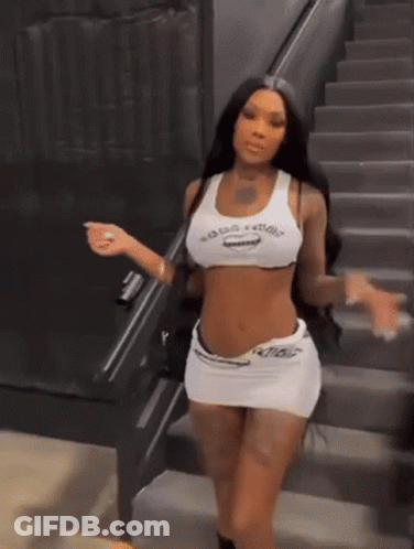 A Woman Is Standing On A Set Of Stairs Wearing A Crop Top And Skirt . GIF