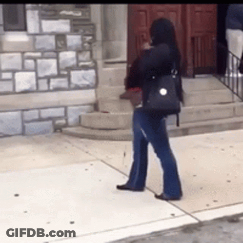 A Woman Is Standing On A Sidewalk In Front Of A Building GIF