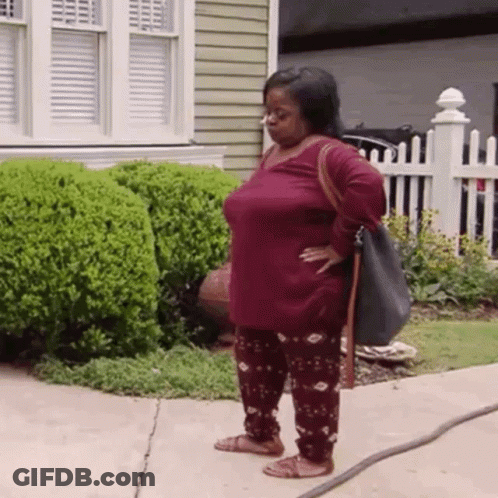 A Woman Is Standing On A Sidewalk In Front Of A House Holding A Hose . GIF