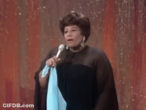 A Woman Is Standing On A Stage Holding A Microphone And A Blue Cloth . GIF