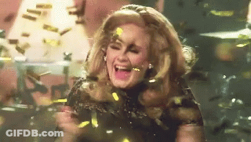 A Woman Is Standing On A Stage Surrounded By Confetti And Laughing . GIF