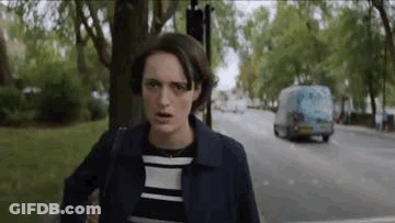 A Woman Is Standing On The Side Of A Street Looking At The Camera . GIF