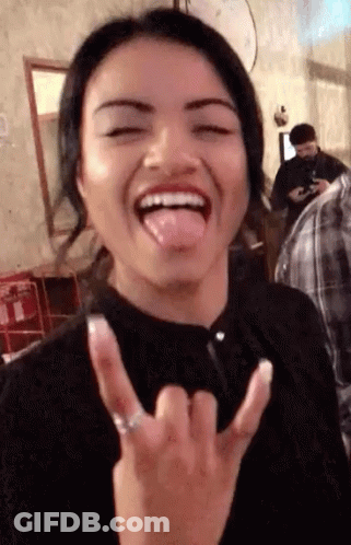A Woman Is Sticking Her Tongue Out And Making A Devil Horns Gesture GIF