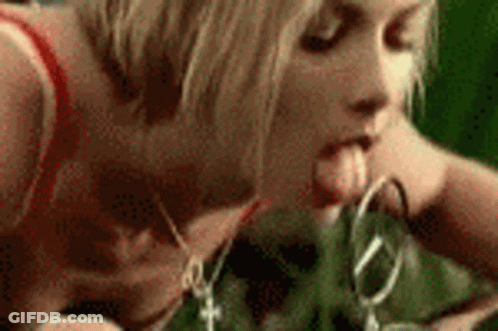 A Woman Is Sticking Her Tongue Out While Holding A Pair Of Scissors In Her Mouth . GIF