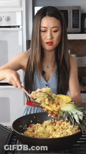 A Woman Is Stirring Food In A Pan With A Pineapple GIF