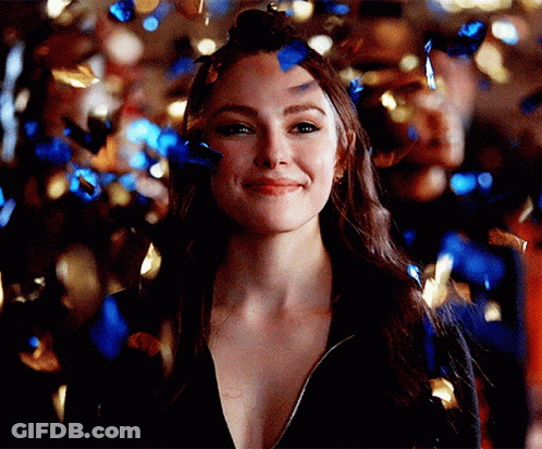 A Woman Is Surrounded By Blue And Gold Confetti And Is Smiling . GIF