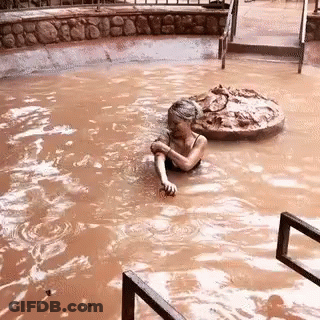 A Woman Is Swimming In A Muddy Pool With A Rock In The Background . GIF