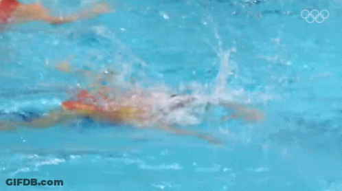 A Woman Is Swimming In A Pool With The Olympic Rings Visible In The Background GIF