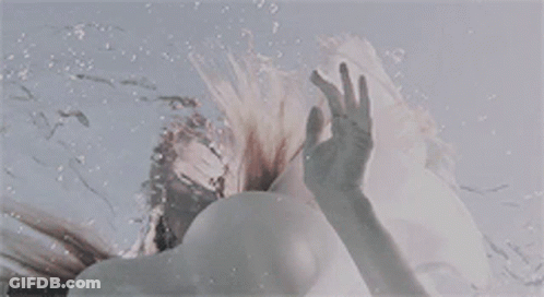 A Woman Is Swimming Underwater And Reaching Out Towards The Sky . GIF