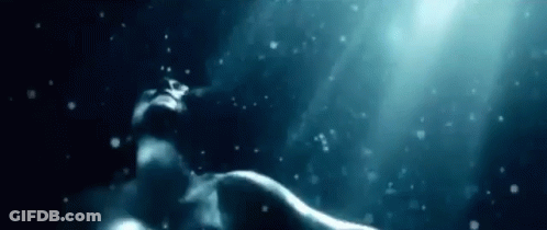 A Woman Is Swimming Underwater In The Ocean With Bubbles Coming Out Of Her Mouth . GIF