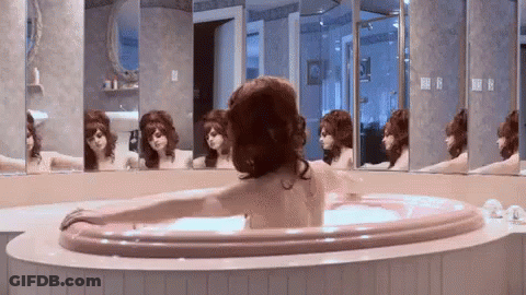 A Woman Is Taking A Bath In A Jacuzzi In Front Of A Mirror . GIF
