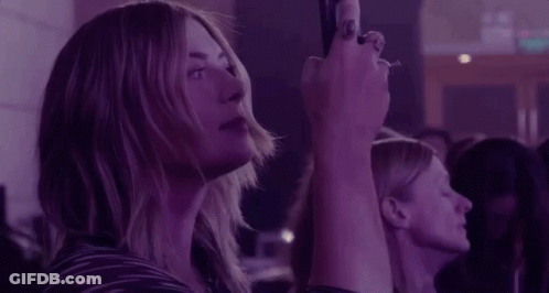 A Woman Is Taking A Picture Of A Crowd Of People At A Concert . GIF