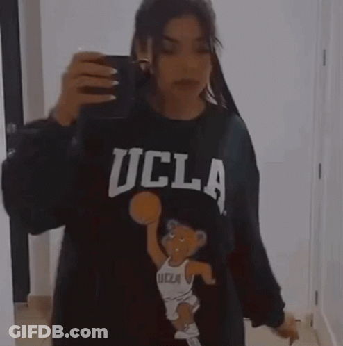 A Woman Is Taking A Picture Of Herself In A Mirror While Wearing A Ucla Sweatshirt . GIF