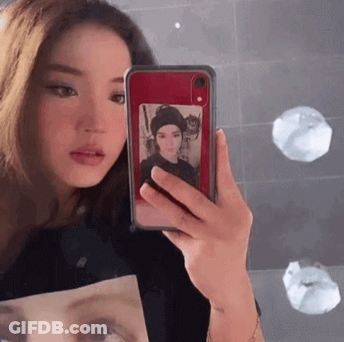 A Woman Is Taking A Picture Of Herself In A Mirror With Her Phone . GIF